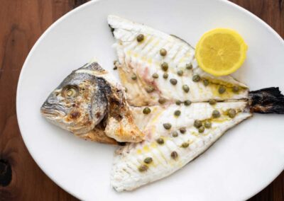Whole Fish with capers and lemon on white plate